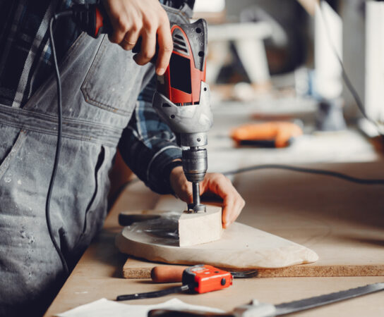 The carpenter works with a tree A man carves a tree. The carpenter works with a drill in a studio. An engineer provides a tree shape